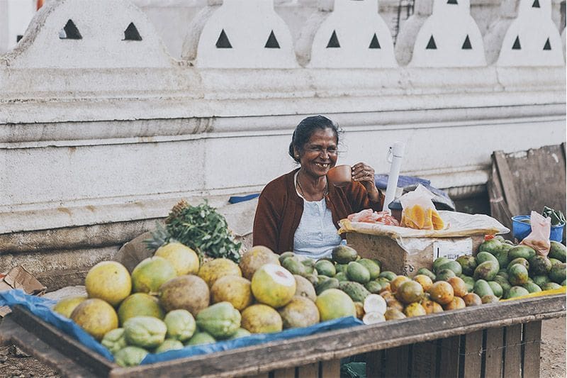 mujer local de Sri Lanka bebe te y sonrie en su puesto de fruta