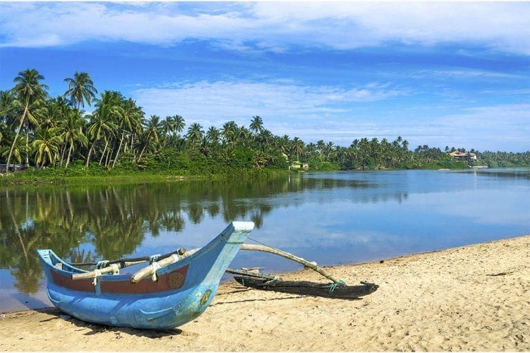 paisaje del rio Bentota y la arena de la playa con un barco de pescador y cielo azul en la costa oeste de Sri Lanka