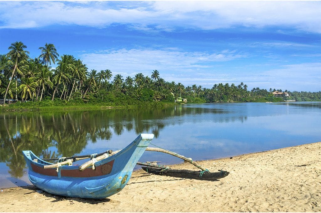 paisaje del rio Bentota y la arena de la playa con un barco de pescador y cielo azul en la costa oeste de Sri Lanka